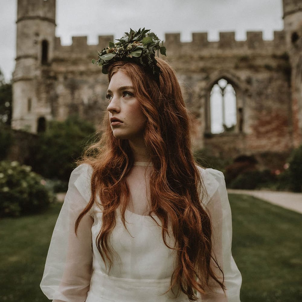Bride in a wedding dress with sheer top layer wearing a foliage flower crown standing in the gardens at Bishop's Palace, Wells