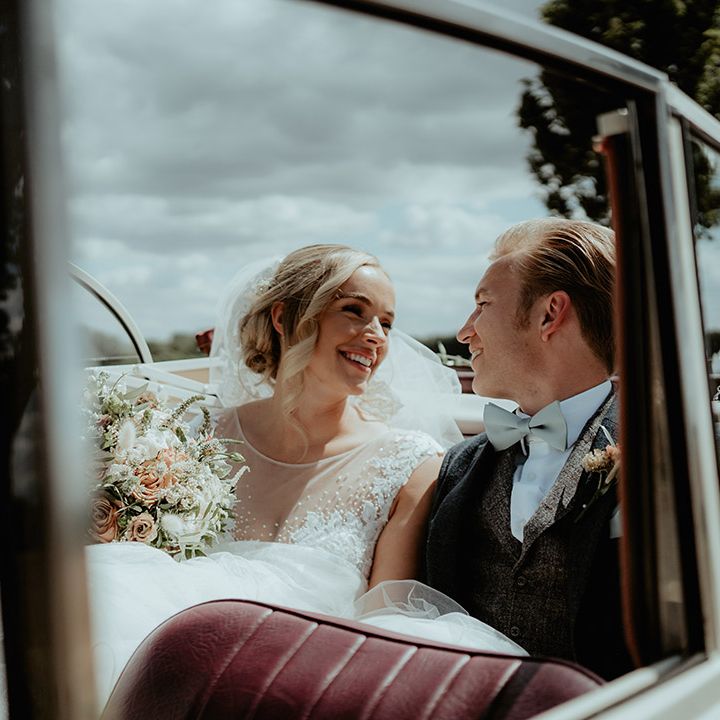 Bride and groom smile at each other and look into each other's eyes as they ride in their wedding car 