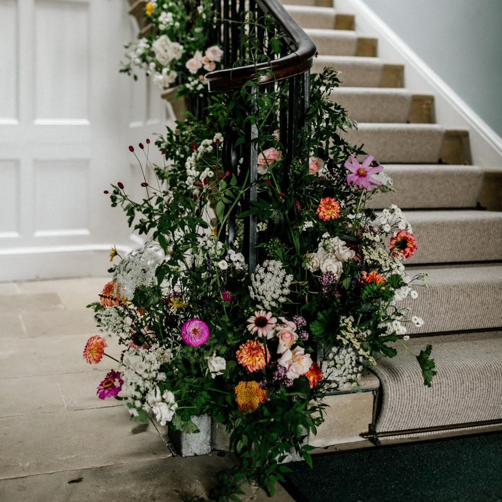 Grand staircase with large foliage and neutral coloured floral display at one of the best country house wedding venues