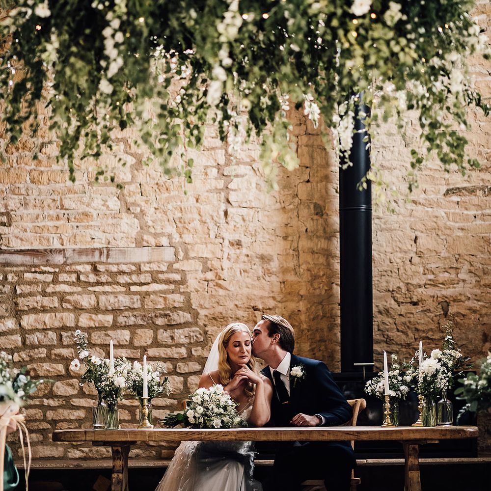 Groom kisses the bride on the cheek as they sit together to sign the register at the Old Gore Barn
