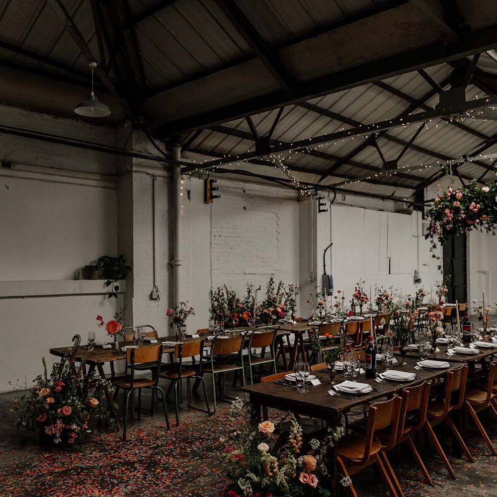 Neutral, minimalistic wedding tablescapes at Hackney Studios with large foliage decor with pops of colour, tapered candles and confetti on the floor