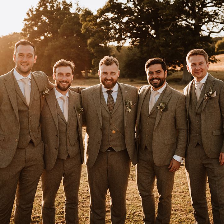 The groom and the groomsmen during golden hour all in matching grey tweed three piece suits