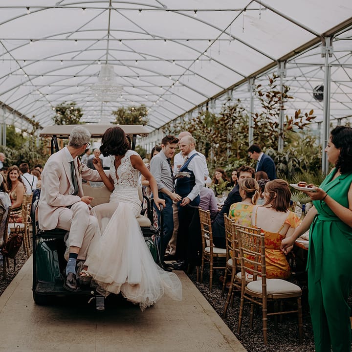 Bride and Groom sit on buggy looking behind them with brides tulle fishtail dress hanging off the edge