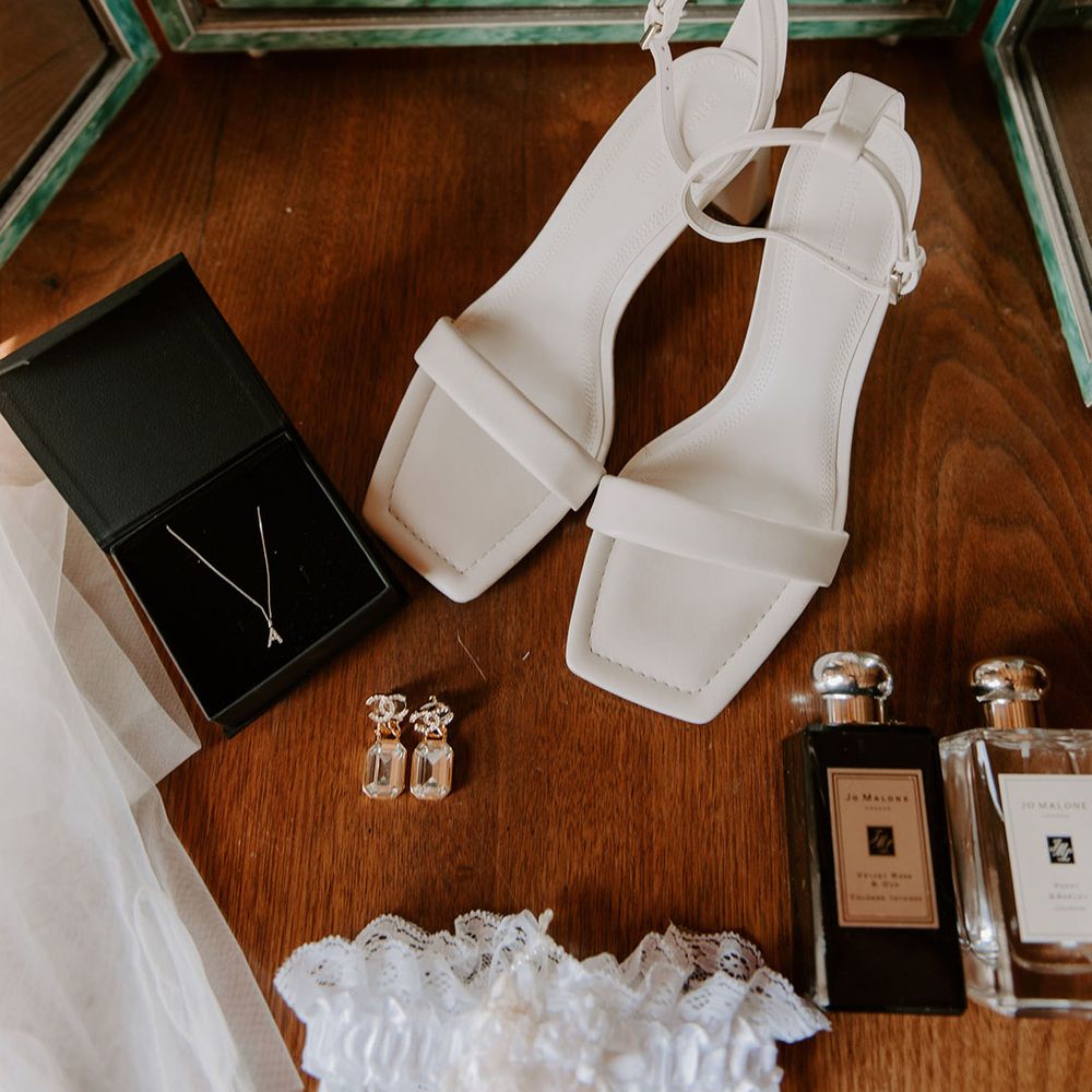 Square toe plain white shoes with Chanel earrings, initial necklace, Jo Malone perfume, and garter for the bride 