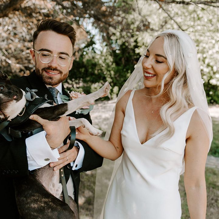 The bride and groom give their pet dog some love who wears a bow tie 