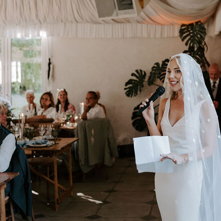 Bride in a white Made With Love wedding dress with a flower applique veil reading out her speech