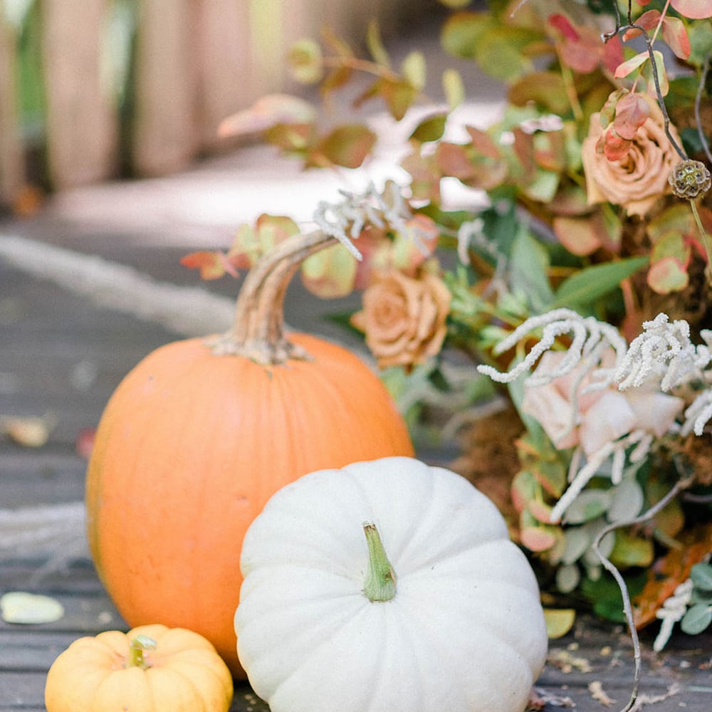 White, yellow and orange pumpkin decor in front of wedding florals 