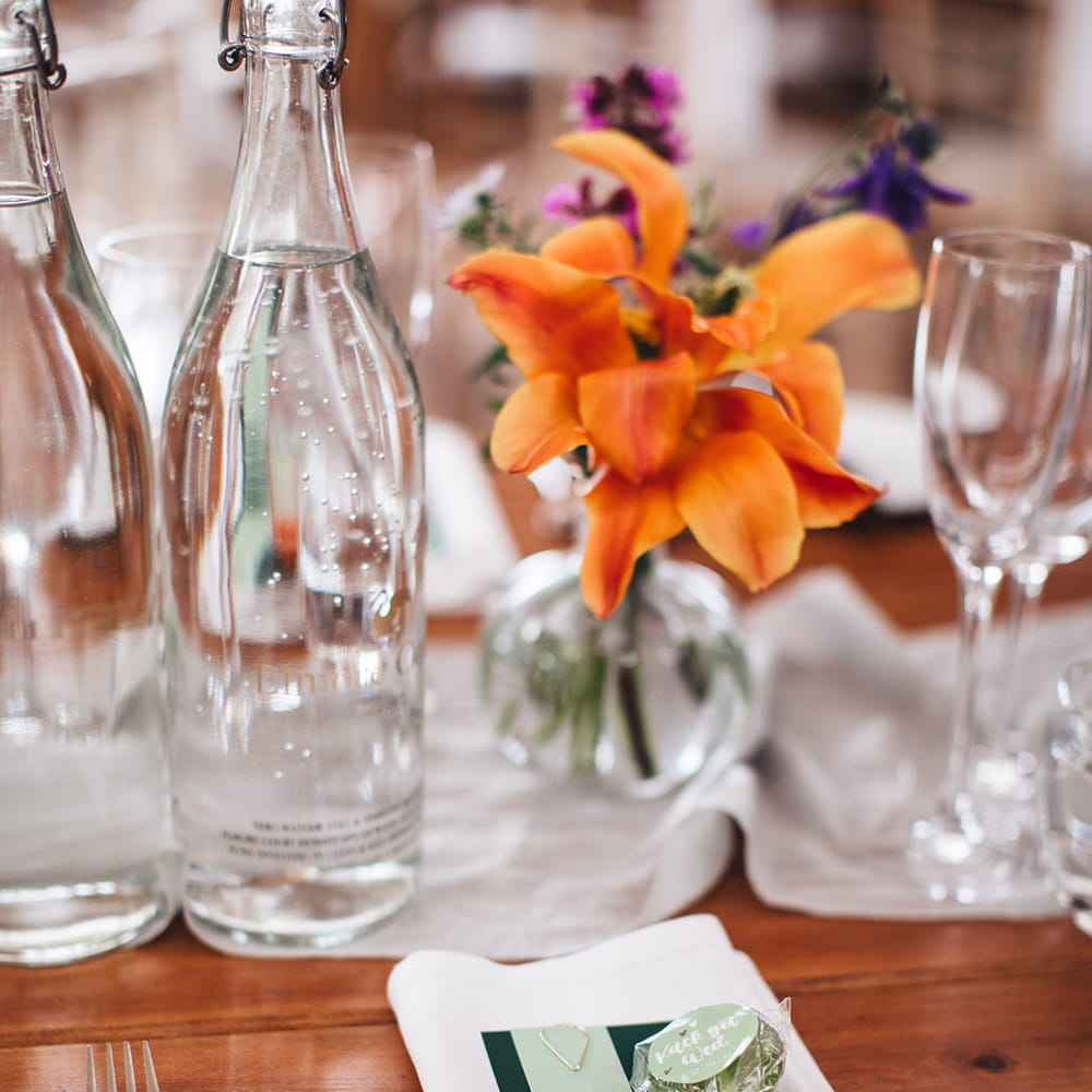 White napkin with dark green menu and light green wedding place name with a green lollipop wedding favour with bright orange flower arrangement centrepiece