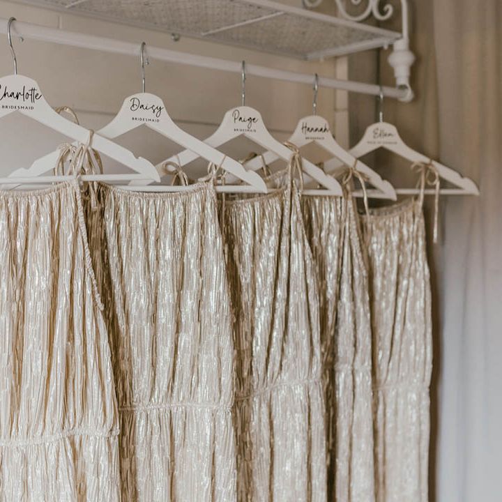 The bridesmaid's shimmery champagne gold bridesmaid dresses hanging on a personalised white hanger 