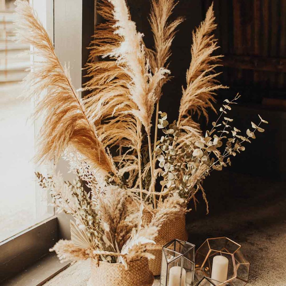 Pampas grass and eucalyptus wedding flower arrangements in wicker vases next to pillar candles in geometric glass candle holders 