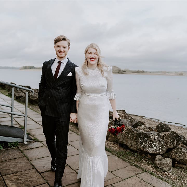 Groom in pinstriped suit walking with the bride in a metallic silver wedding dress with shoulder pads and ruffle detail 