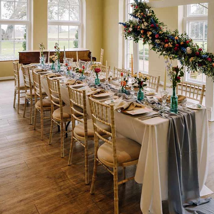 Classic wedding tablescape at Braxted Park wedding venue with white wedding tablecloth, cornflower blue wedding table runner, bright blue glass bottles with dried flowers, pastel tapered candles and spring floral arrangements 