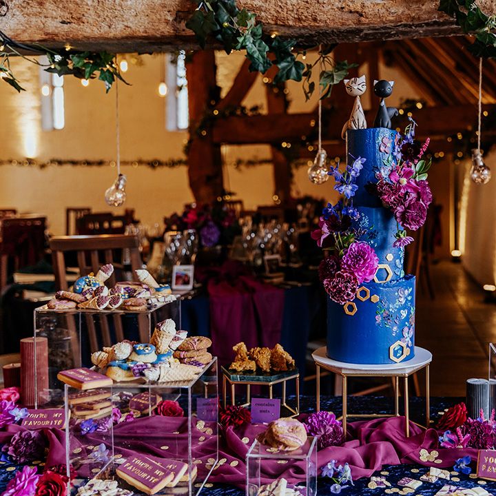 Dark blue wedding cake decorated with cat cake topper on a dessert table with mini ice cream cones, biscuits, flapjacks and more 