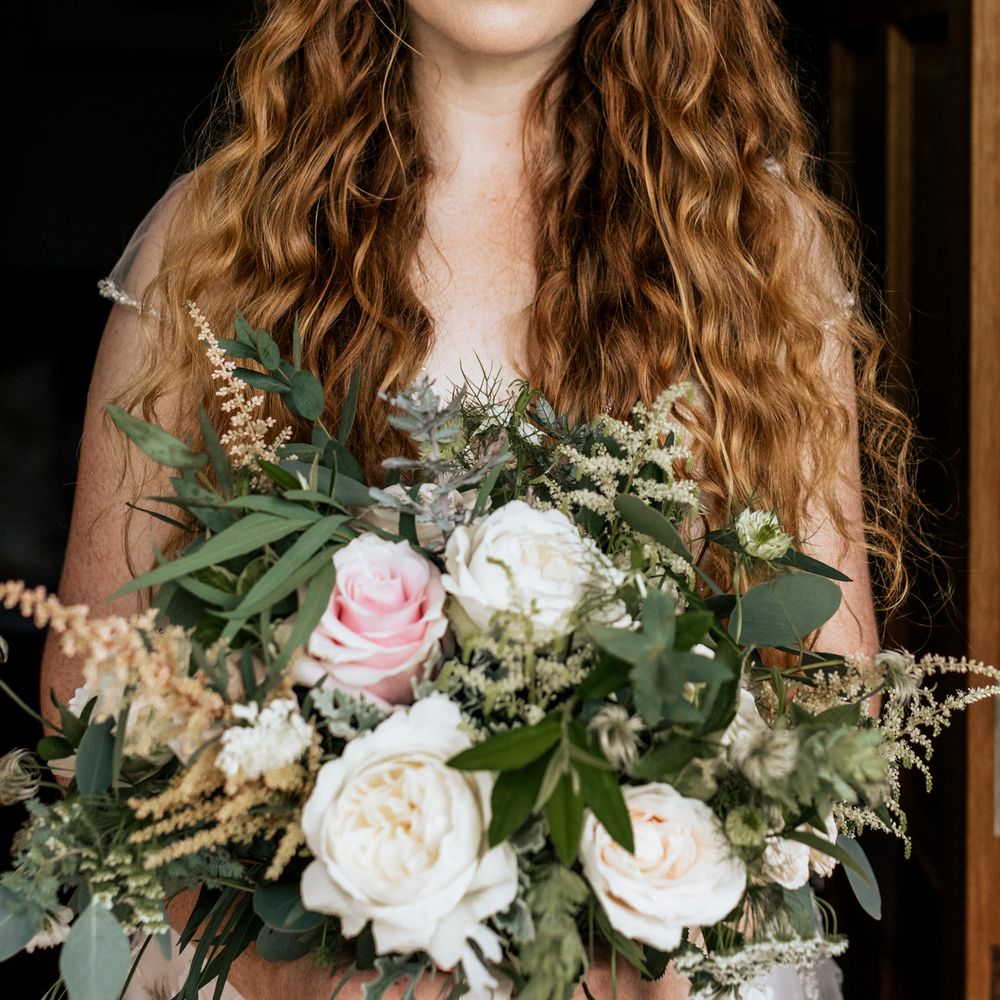 Bride wearing appliqué wedding dress holding floral bouquet with pink roses