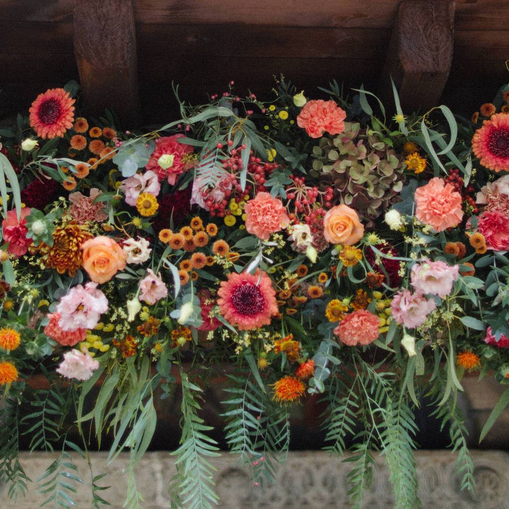 A large centrepiece flower display of orange, red and pink blooms, including carnations, roses and daisies