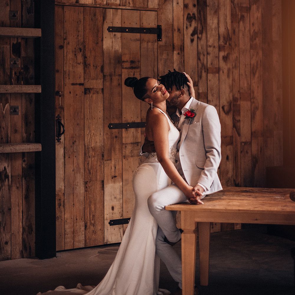Groom sits on table as bride embraces him 
