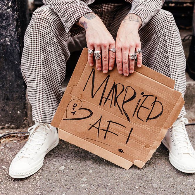 Groom in a check suit and trainers holding a card board sign that says Married AF