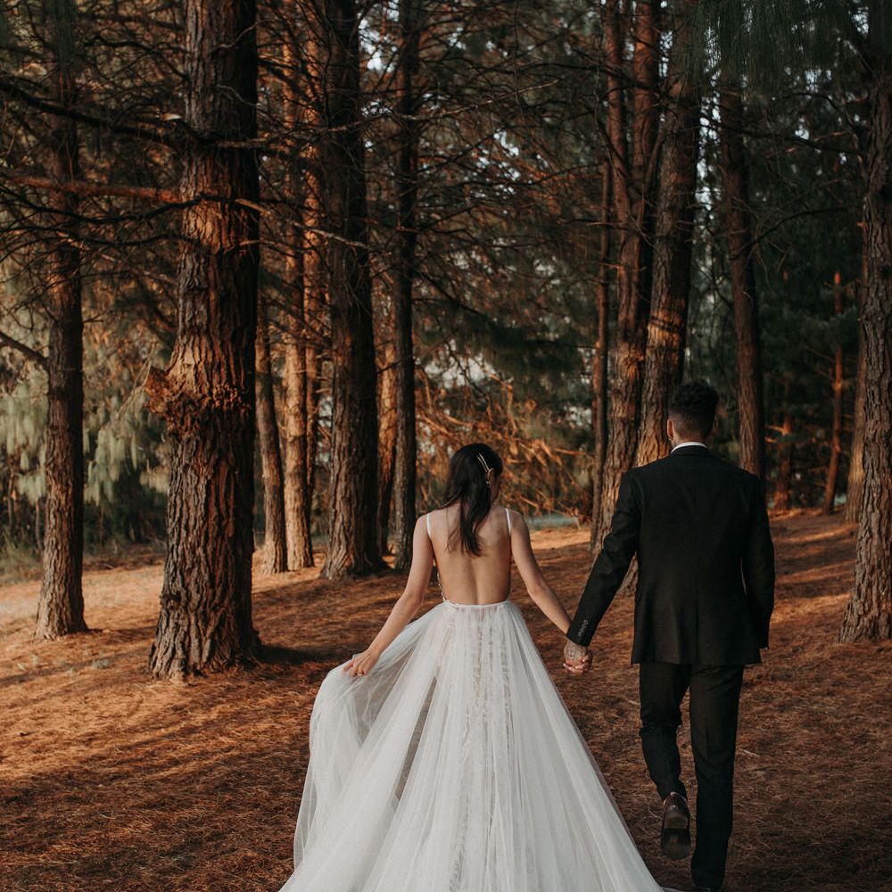 Bride in a fitted lace wedding dress with detachable chiffon shirt talking in the woods with her husband 