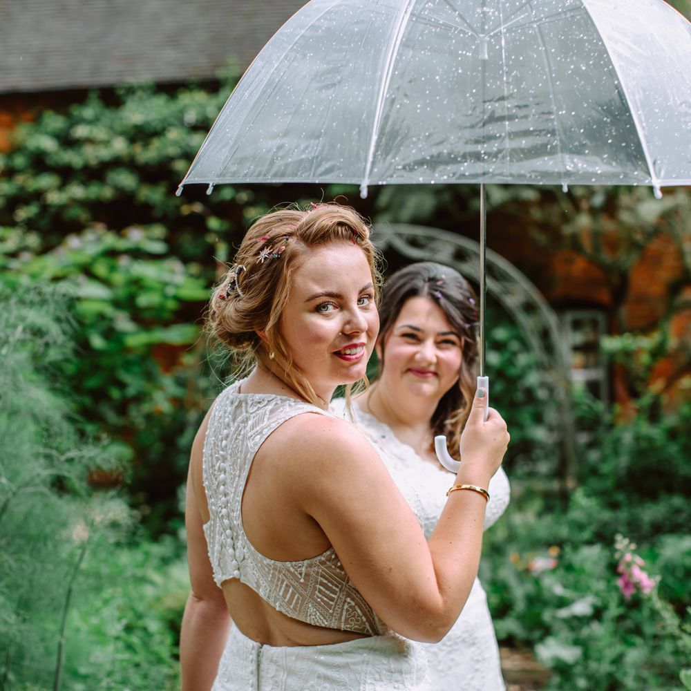 Lesbian brides stand under umbrella together on their wedding day for Park Farm wedding