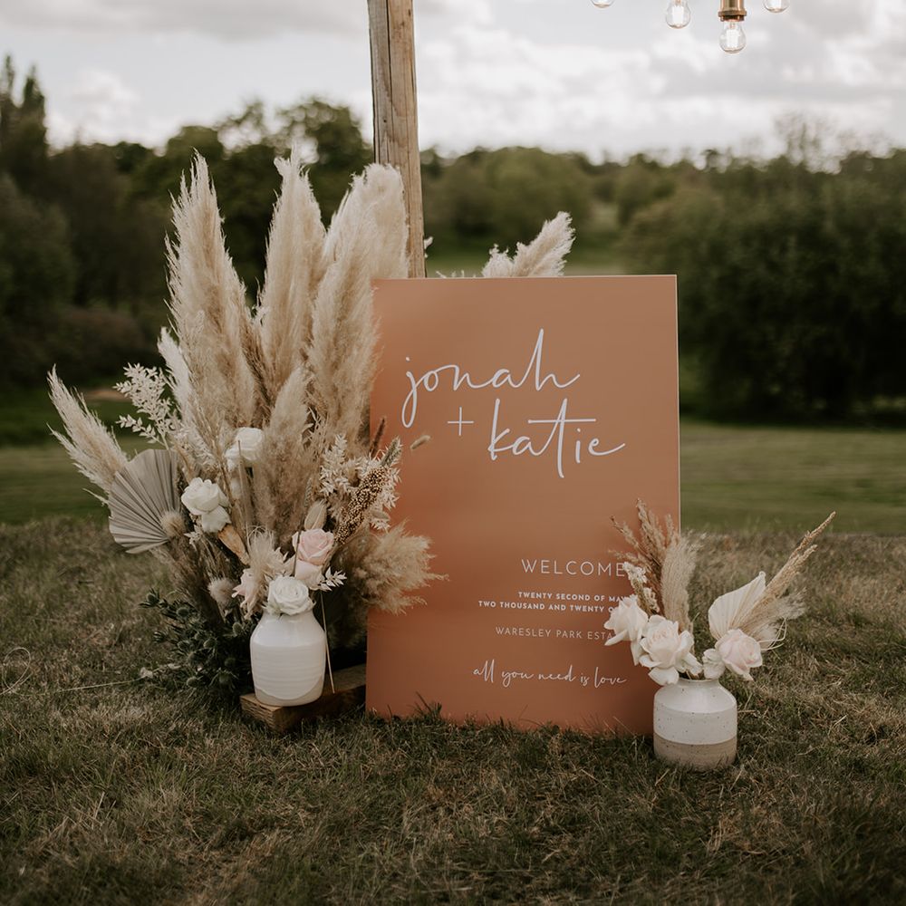 Terracotta wedding welcome sign surrounded by dried and fresh flower arrangements with palm leaves and pampas grass 