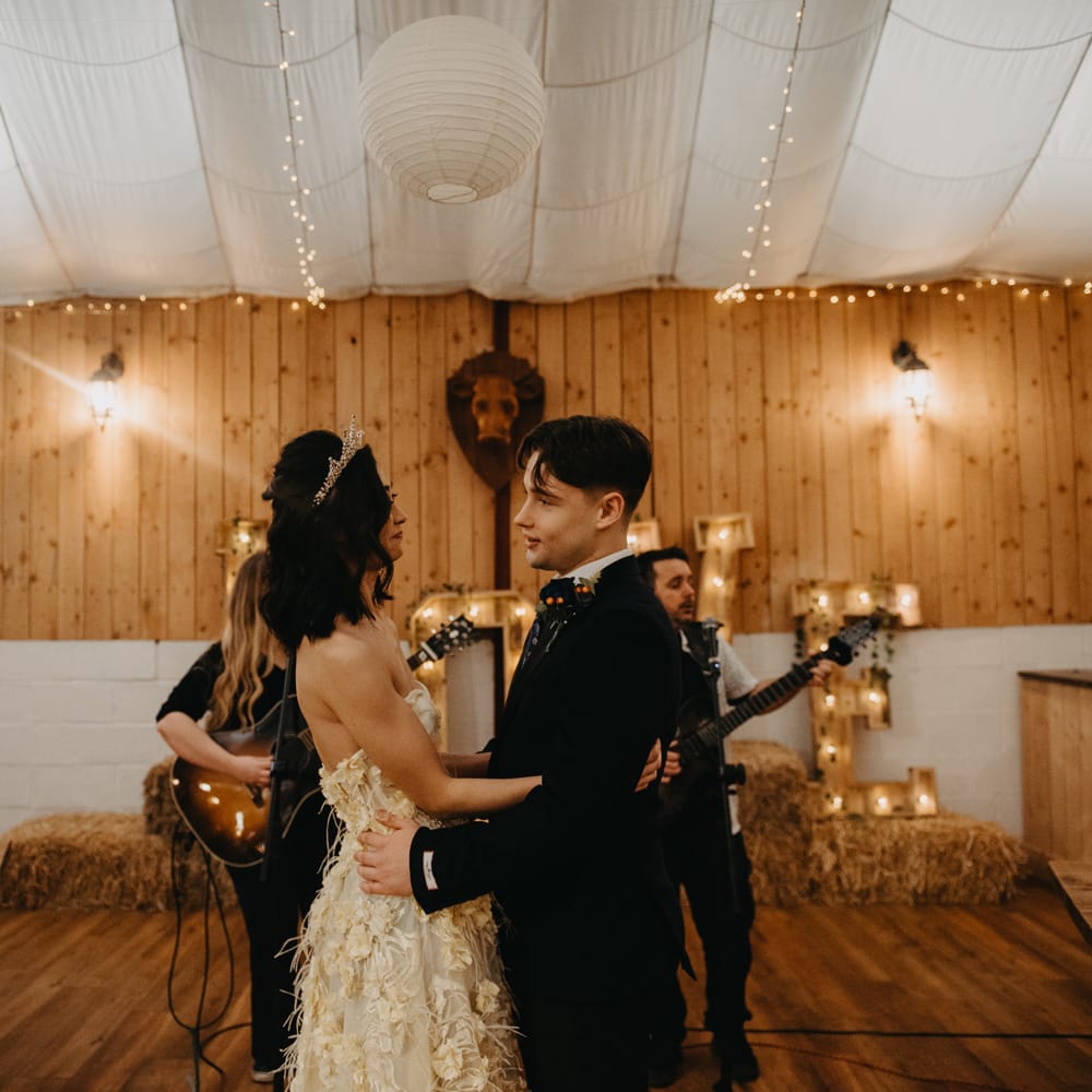 Bride in strapless feathered wedding dress and headpiece hugs groom in dark blue suit during Wellbeing farm wedding ceremony in Lancashire