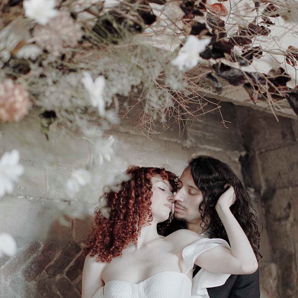 Groom with long hair kissing his bride with red naturally curly hair in a strapless wedding dress at Blackfriars Priory 