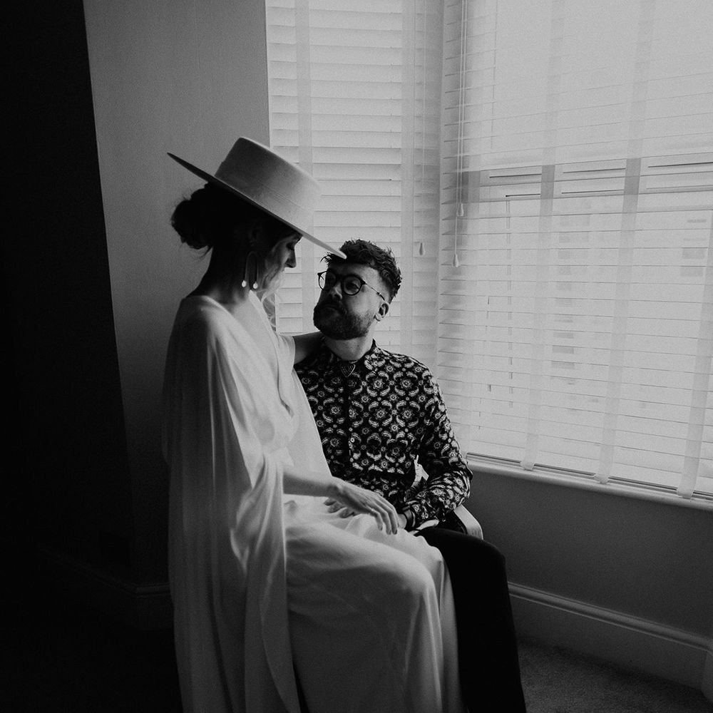 Black & white image of bride and groom sat by window