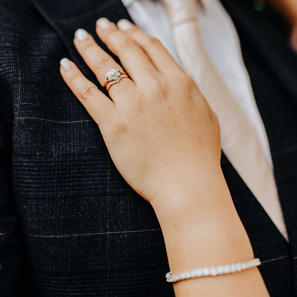 Bride wears flower shaped diamond wedding ring as she places hand on grooms check suit