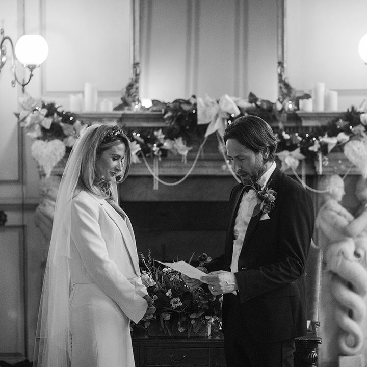 Bride & groom stand in front of fireplace complete with wreath on their wedding day