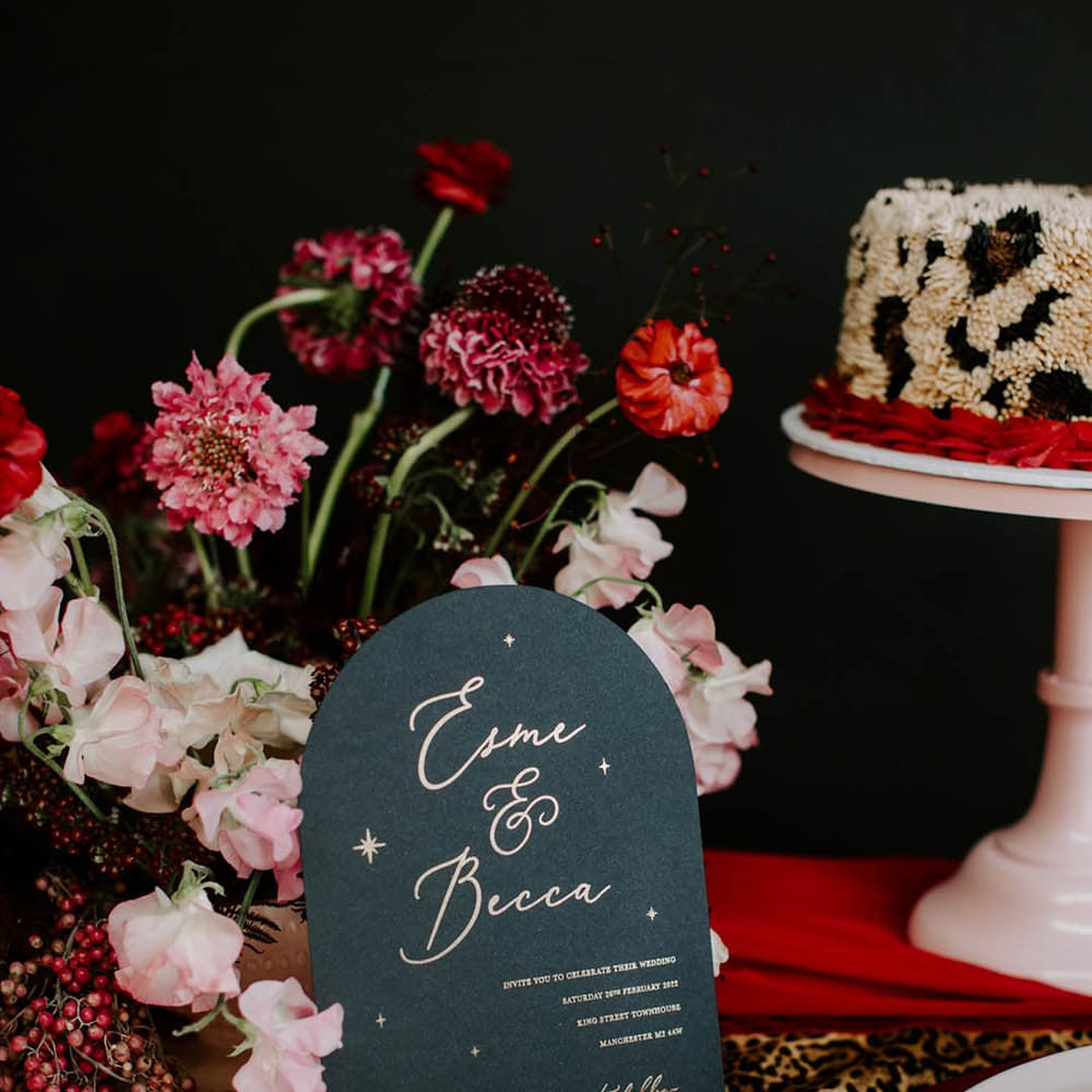 Leopard print buttercream wedding cake and black wedding invitation ith gold foil lettering and red tassel 