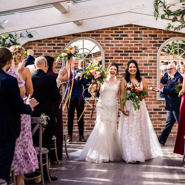 Bride in lace mermaid style tulle wedding dress with bride in floral lace wedding dress walk back down the aisle together 