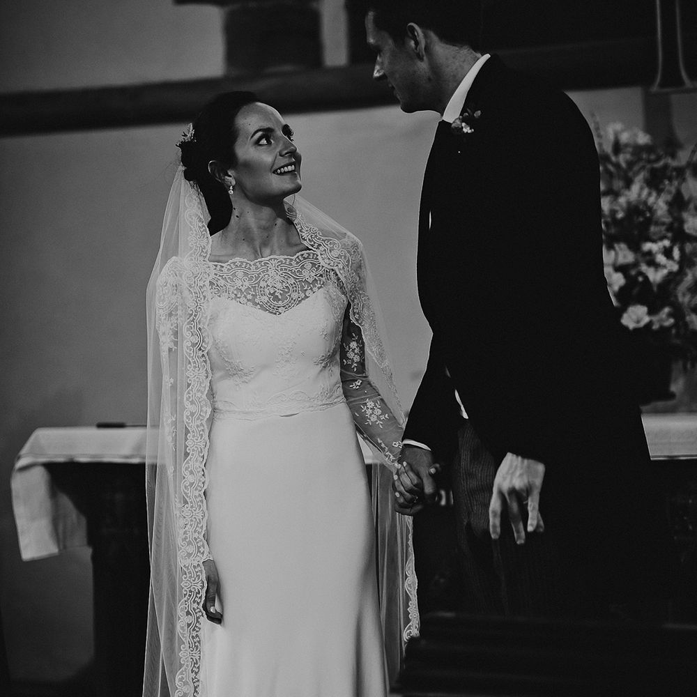 Bride in satin wedding dress with lace detail and sheer long sleeves holding hands with groom after traditional church wedding ceremony 