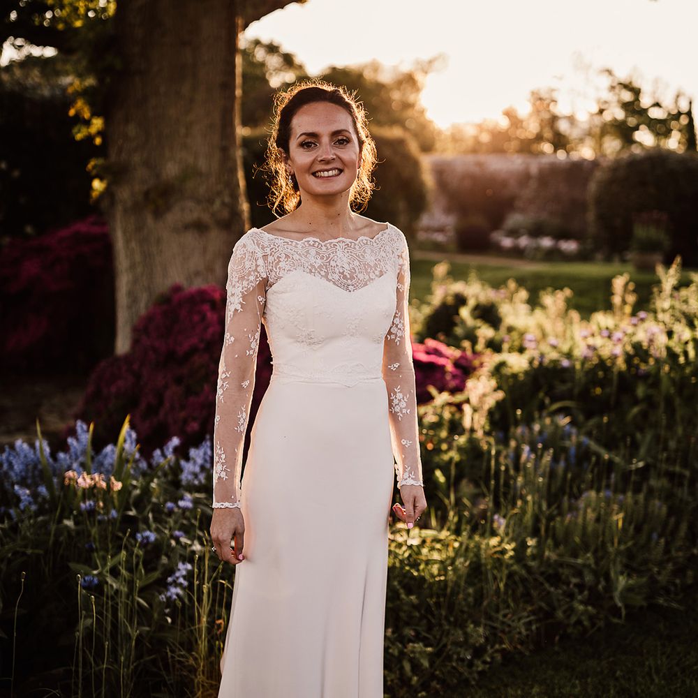 Bride in satin wedding dress with lace top and sheer long sleeves holding colourful wedding bouquet
