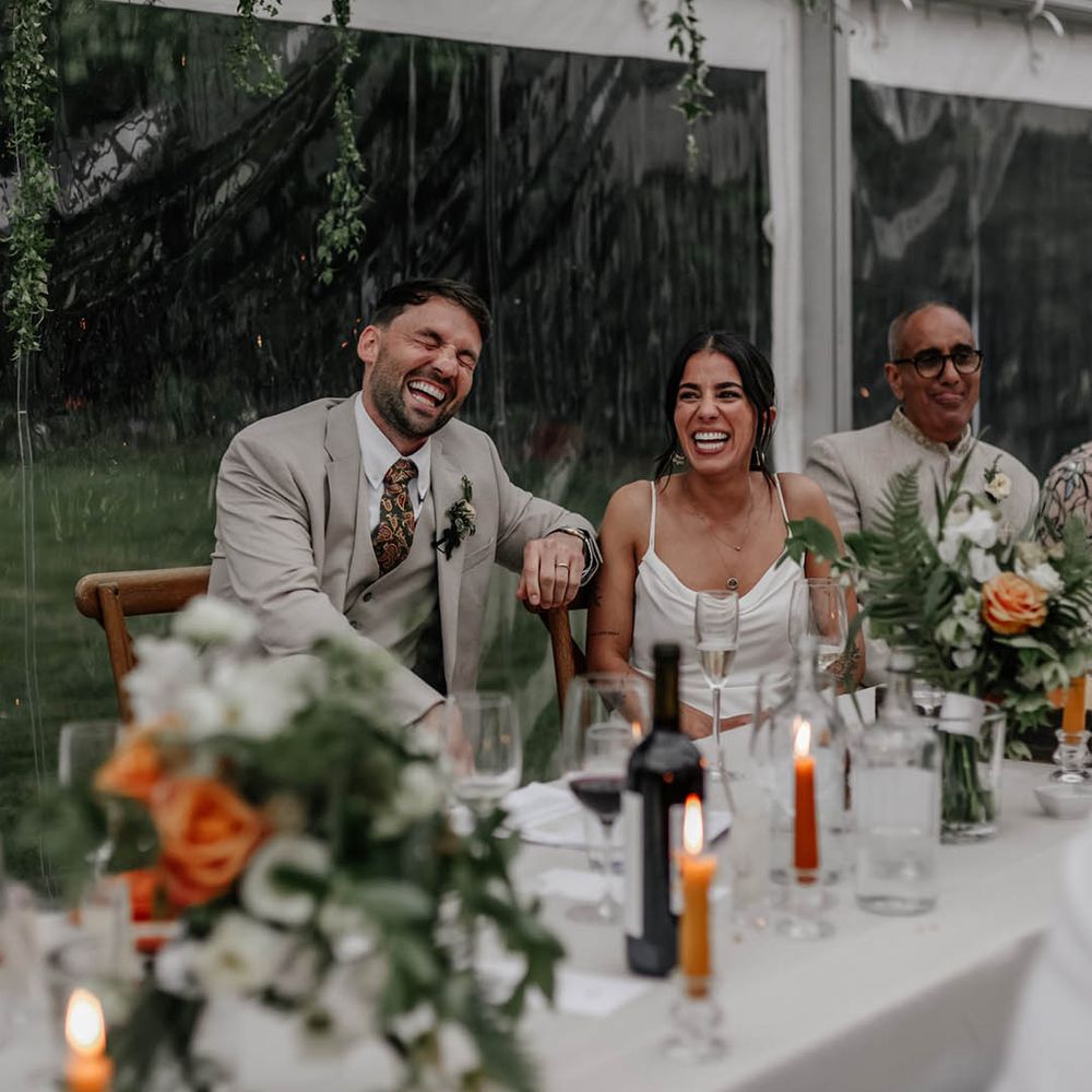 Bride and groom laughing during the clear marquee wedding reception speeches 