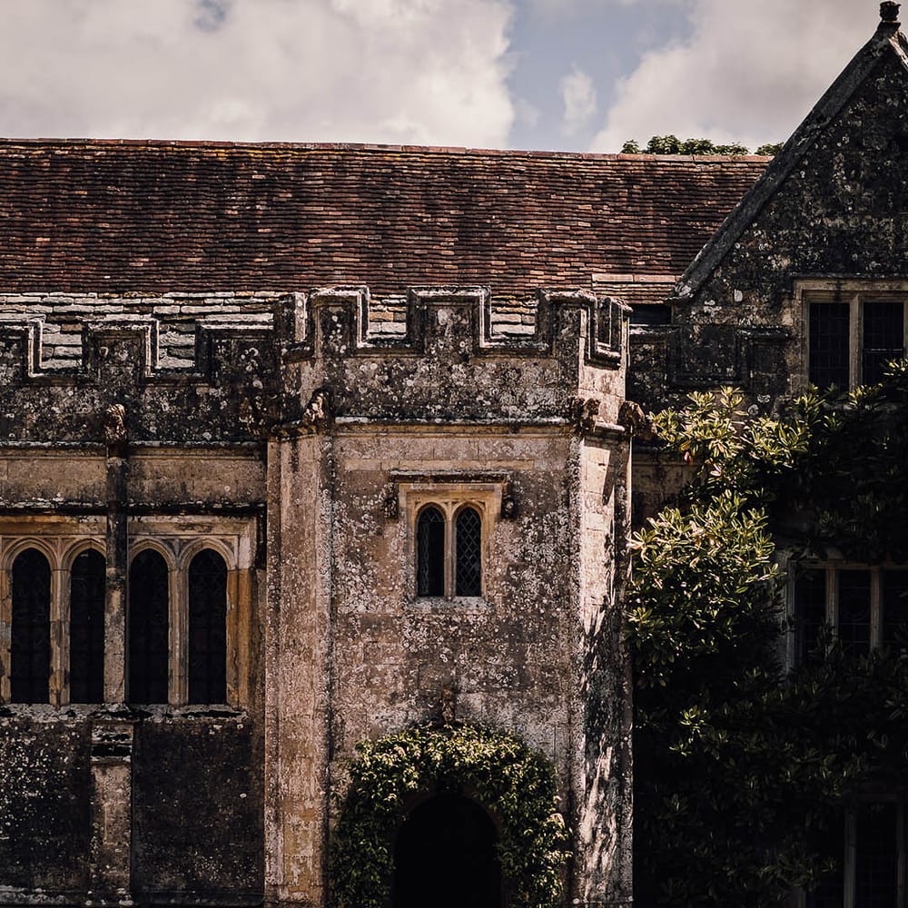 Outdoor wedding ceremony setup with simple green foliage wedding arch and wooden chairs at Athelhampton House 