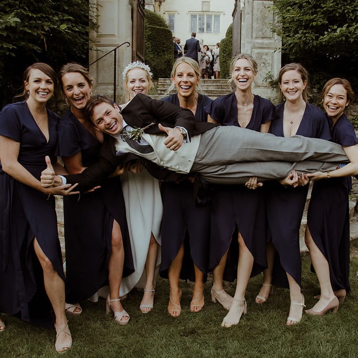 Bridesmaids in navy blue dresses and bride lift the groom together 
