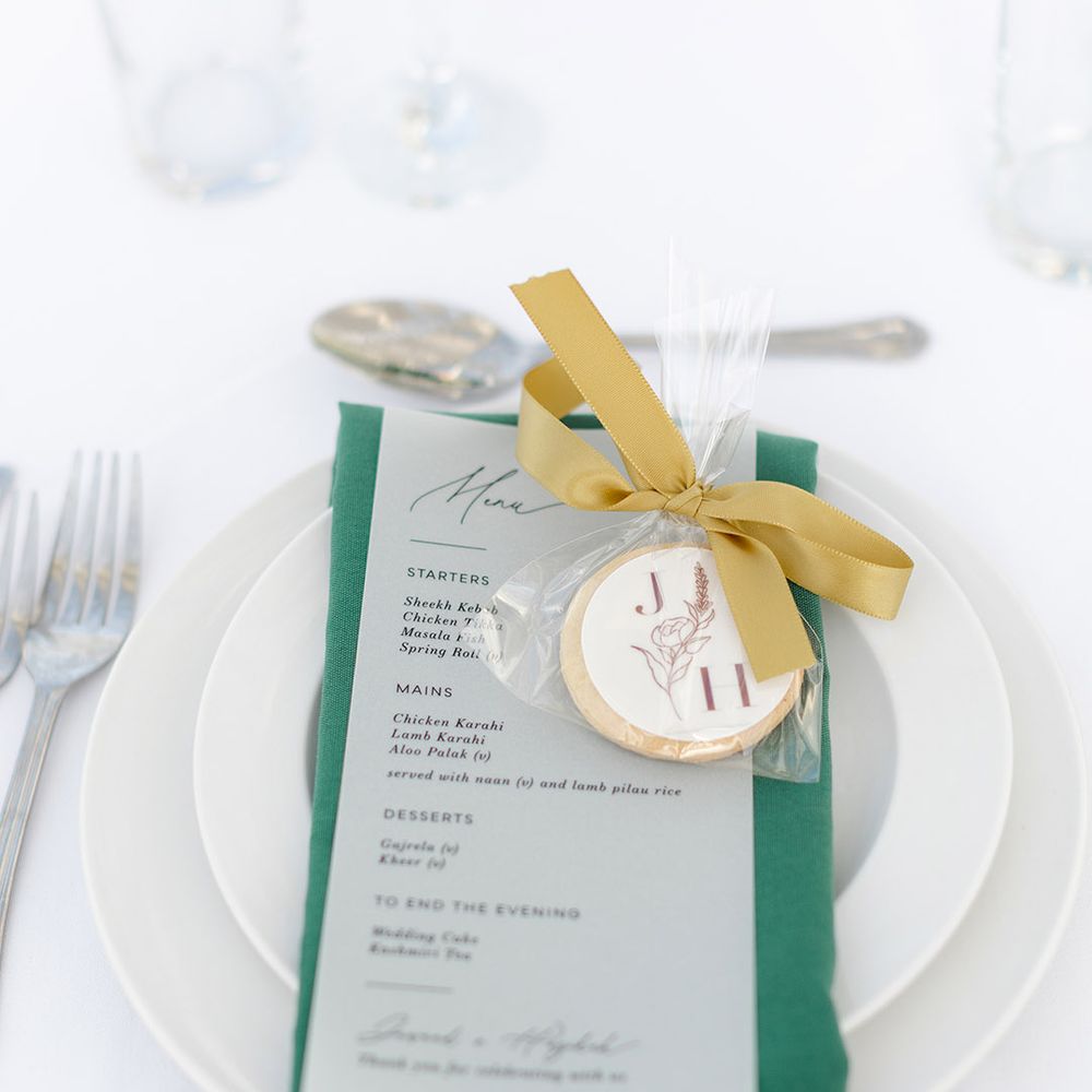 Green napkin sits on white plate complete with gold ribbon and personalised biscuit favours 