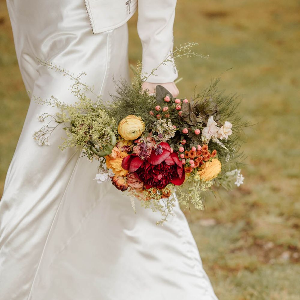 Bride in a satin slip wedding dress holding a red, orange and yellow wedding bouquet with ranunculus 