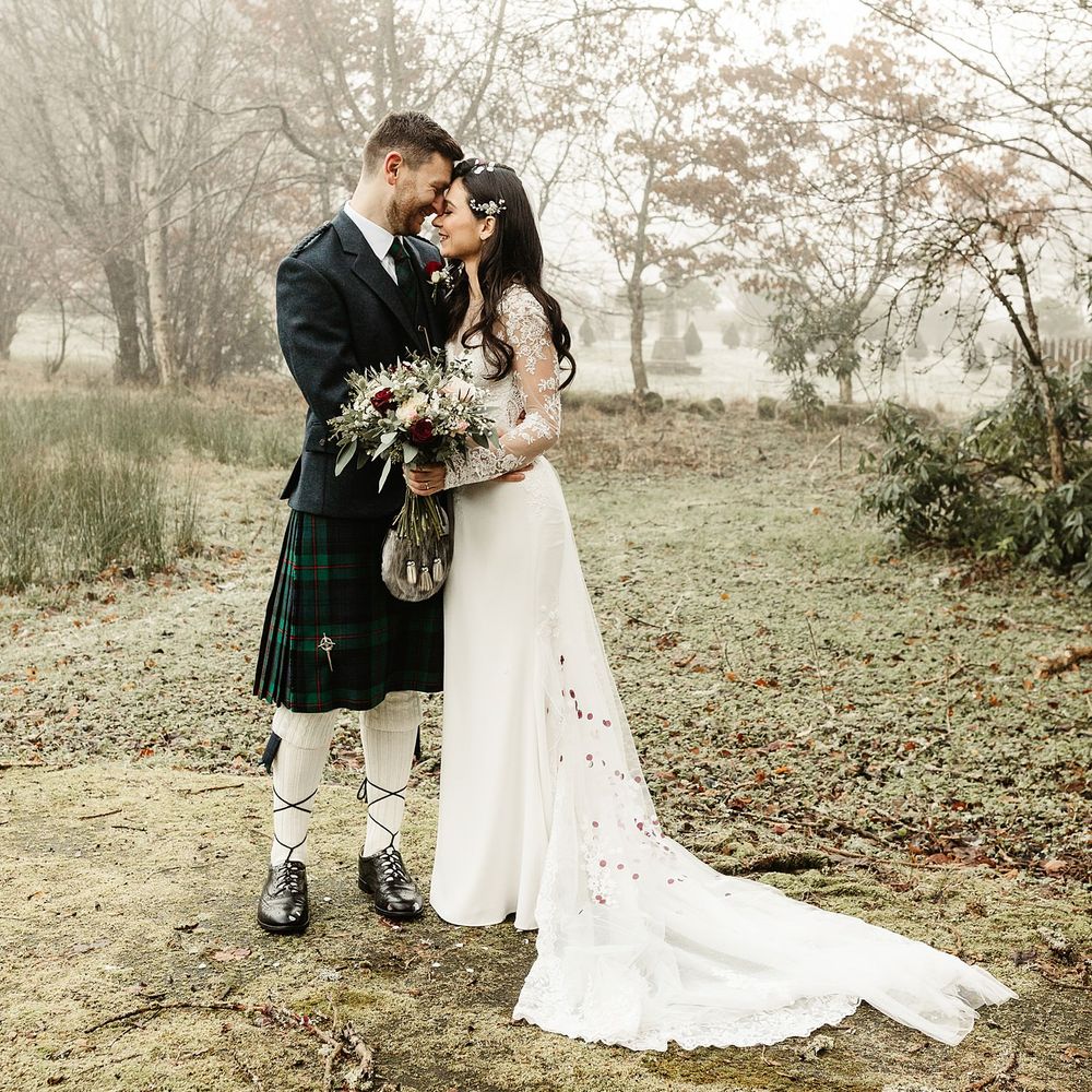 Bride wears lace wedding gown with long sleeves as she holds white and red floral bouquet 