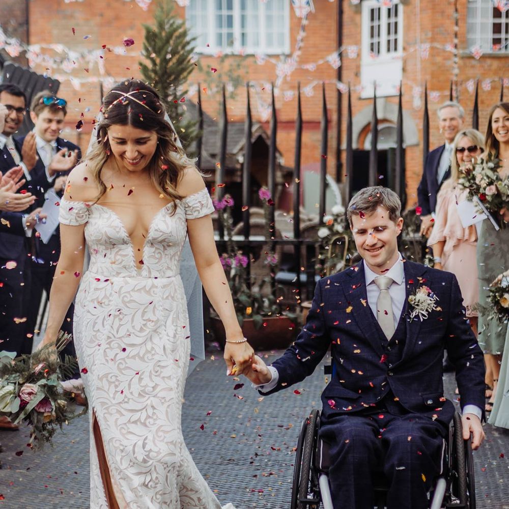 Bride in off shoulder lace wedding dress and groom in dark suit doing confetti throw at Henley Brewery 