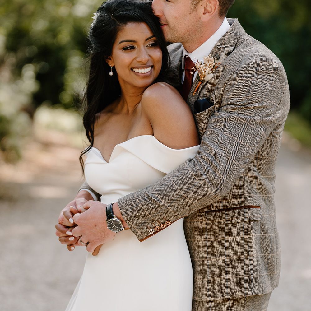 Groom embraces the bride from behind for their wedding at The Great Tythe Barn at Tetbury 