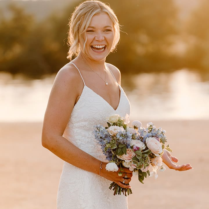 Blonde bride holds pastel floral bouquet and wears lace fitted wedding dress