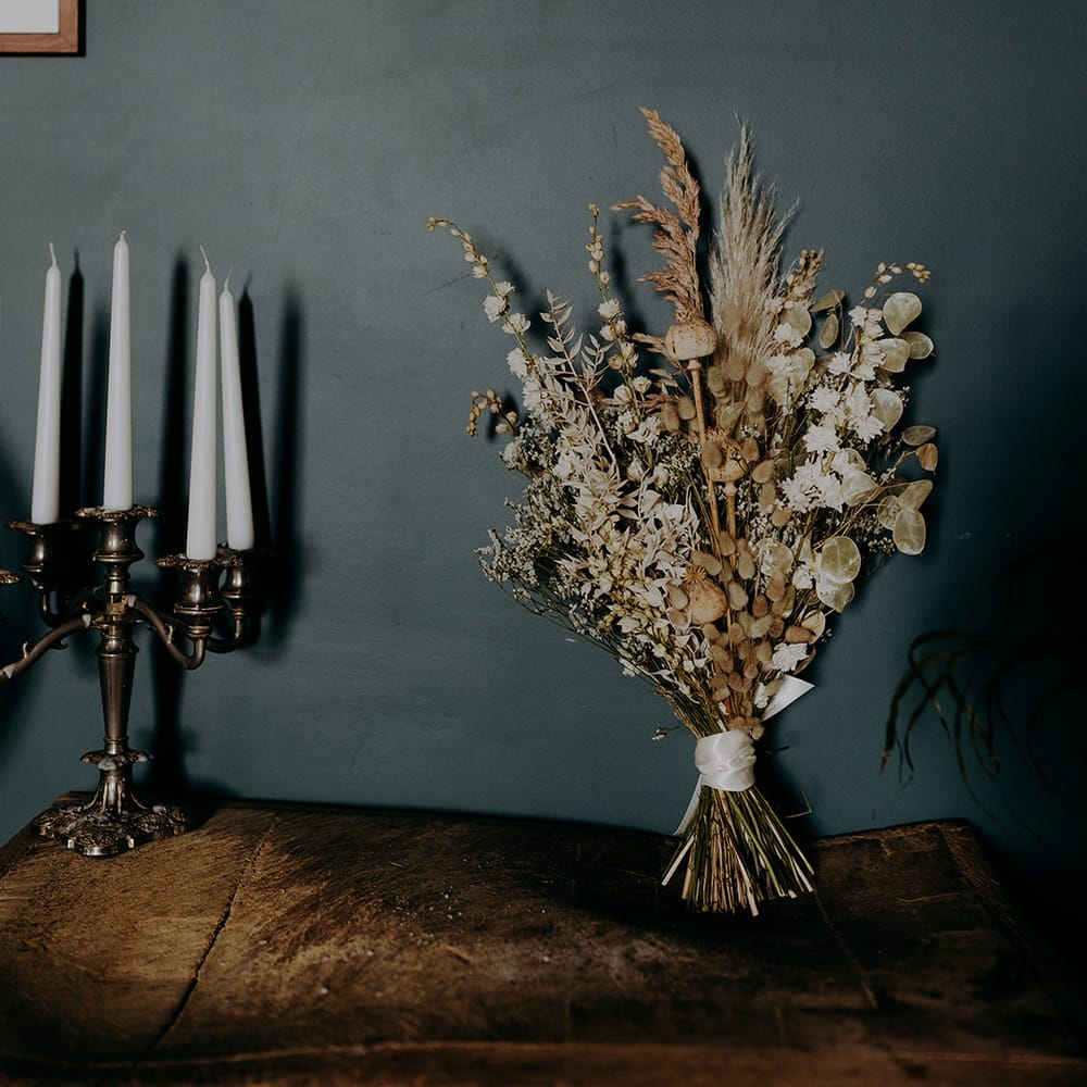 Rustic beige and white dried bouquet leans against dark wall