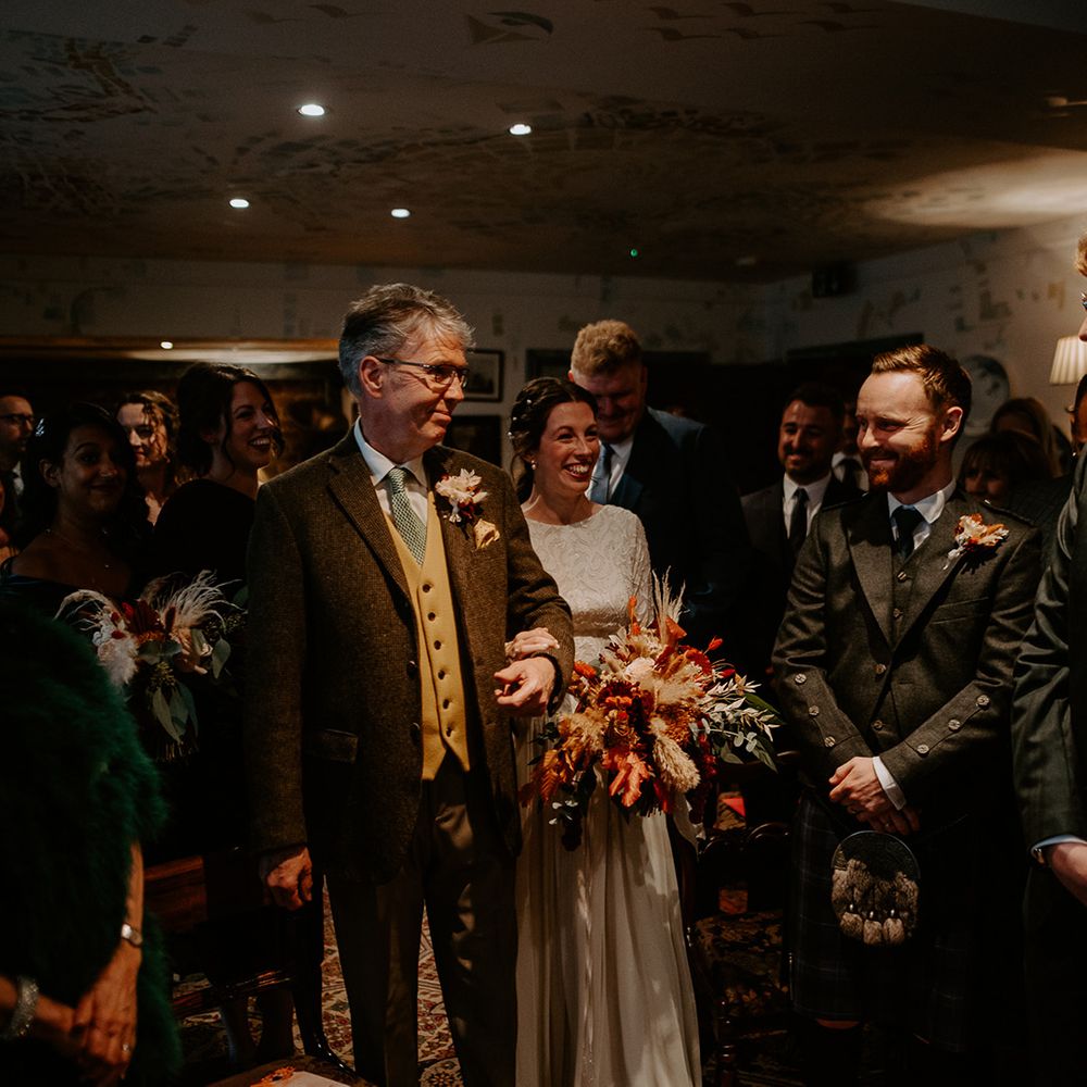 Bride in vintage lace wedding dress holding large autumnal bouquet with roses and pampas grass walking into wedding reception at The Zetter Townhouse