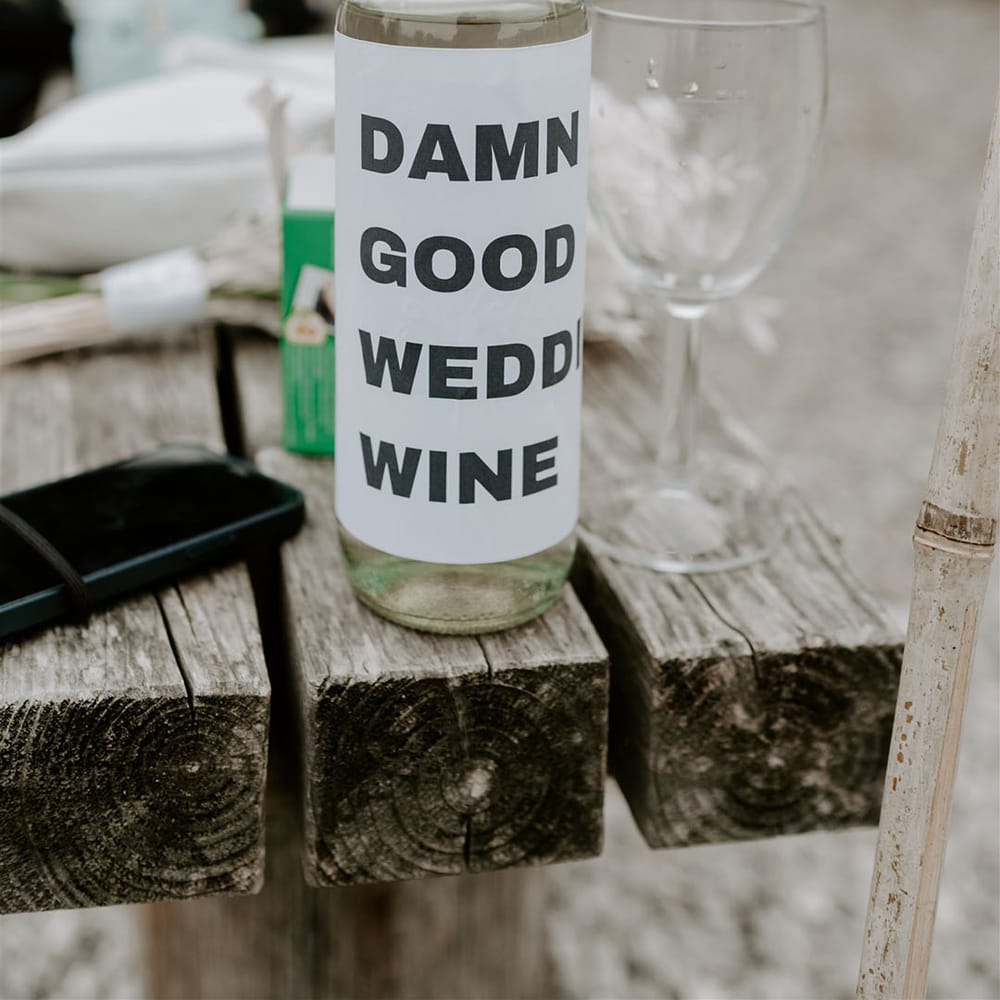 Bottle of white wine covered with white paper reading ' Damn good wedding wine' 