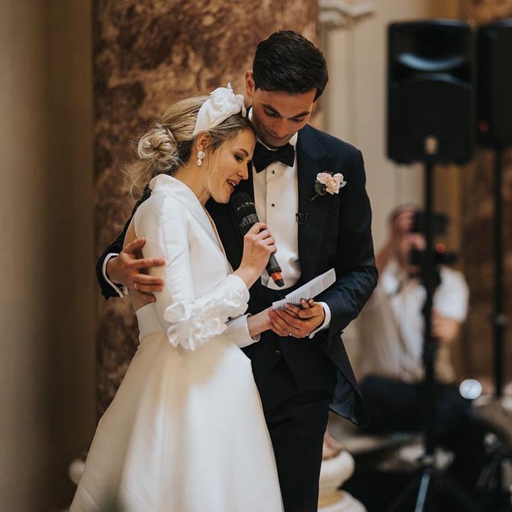 The groom supports the bride as she eats out her wedding speech by embracing her at the wedding reception 