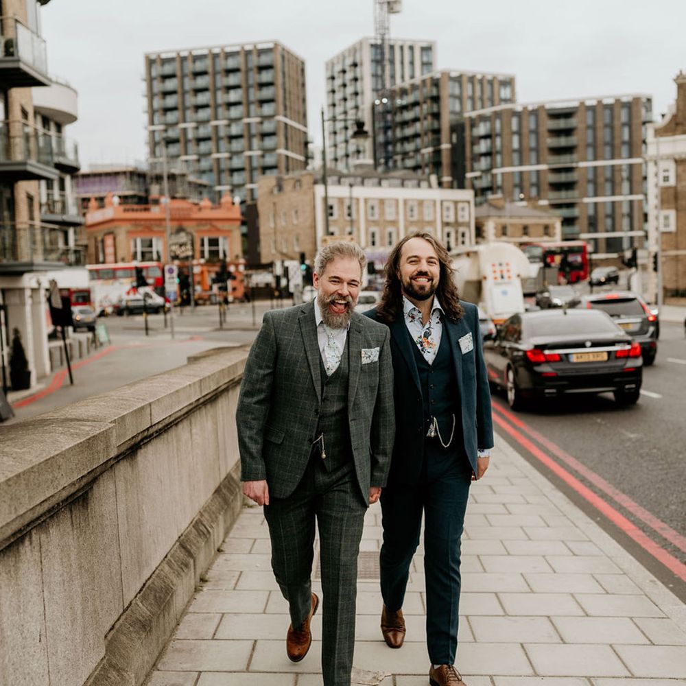 Grooms walk alongside one another in tartan suit and blue suit complete with matching floral tie and shirt and brogues 