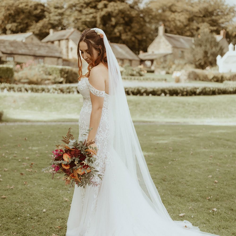 Bride in fitted off the shoulder boho lace wedding dress with embroidered veil for Disney theme wedding 