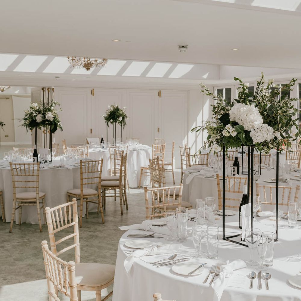 White flower table centrepiece arrangements in tall black metal stands for the monochrome and minimal style wedding at Hayne House 