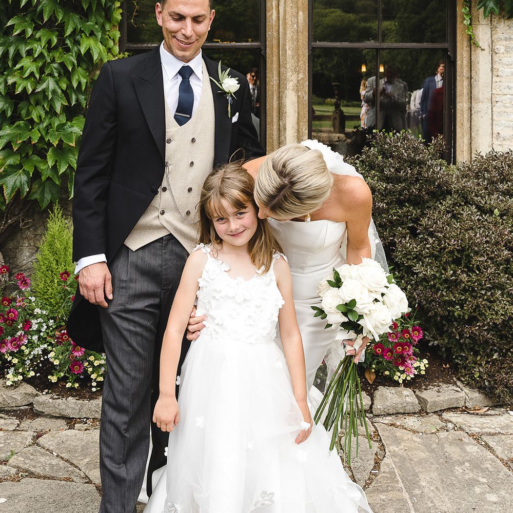 Flower girl in floral tulle dress with the bride and groom on their wedding day 